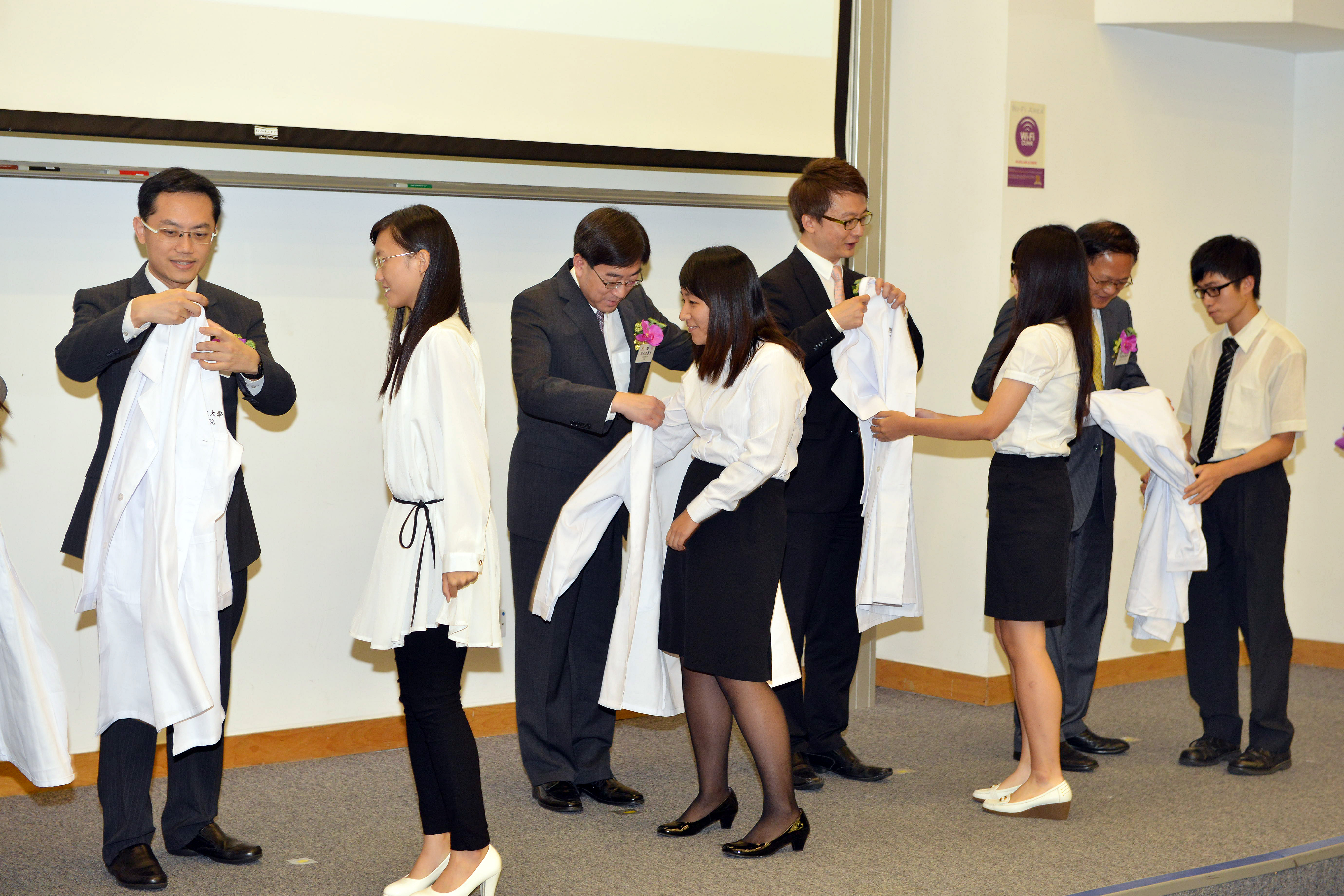 The officiating guests put the white coats on the Chinese medicine freshmen at the White Coat Ceremony.